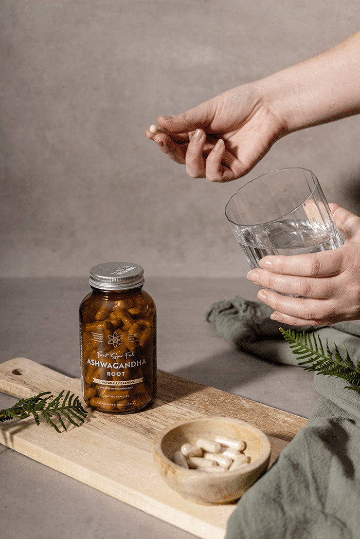 Rest & Relax Bundle showing ashwagandha capsules bottle with a hand holding a capsule and glass of water nearby