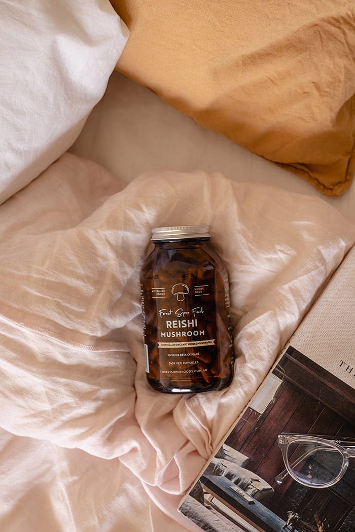 Rest & Relax Bundle with amber jar of organic Reishi Mushroom capsules on soft bedding beside glasses and book